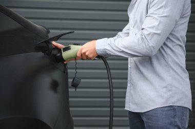 Bir adam elektrikli arabayı şarj eder..