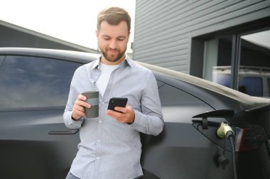 Bir adam elektrikli arabayı şarj eder..