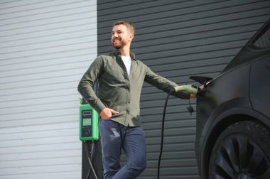 Bir adam elektrikli arabayı şarj eder..