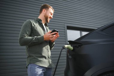 Evin yanında elektrikli araba şarj eden bir adam var..