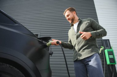 Dışarıdaki otoparkta elektrikli araba için elektrik kablosu tutan adam..