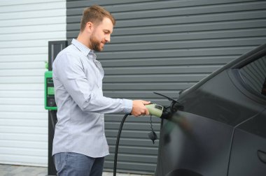 Dışarıdaki otoparkta elektrikli araba için elektrik kablosu tutan adam..