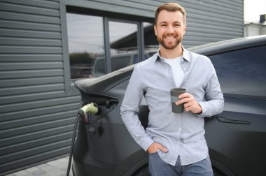 Evin yanında elektrikli araba şarj eden bir adam var..