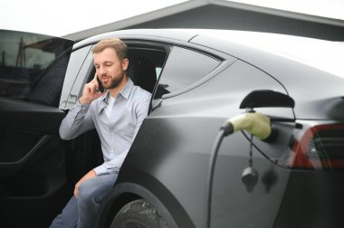 Evin yanında elektrikli araba şarj eden bir adam var..