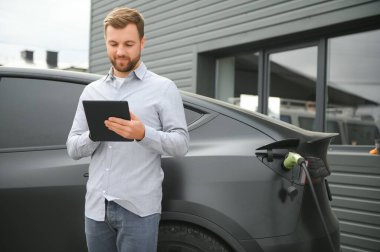 Evin yanında elektrikli araba şarj eden bir adam var..