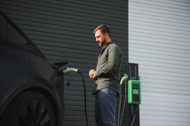 Evin yanında elektrikli araba şarj eden bir adam var..