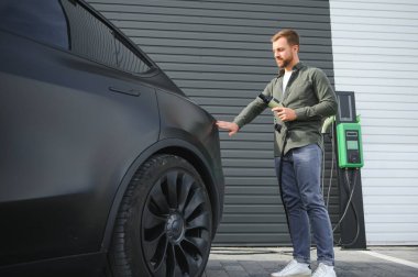 Dışarıdaki otoparkta elektrikli araba için elektrik kablosu tutan adam..
