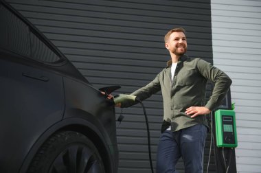 Dışarıdaki otoparkta elektrikli araba için elektrik kablosu tutan adam..