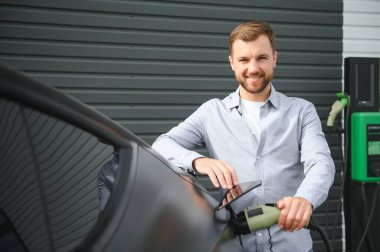 Bir adam elektrikli arabayı şarj eder..