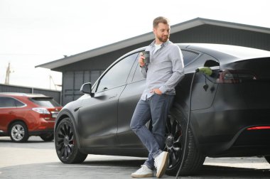 Yakışıklı adam elektrikli araba şarj ederken kahve içme.