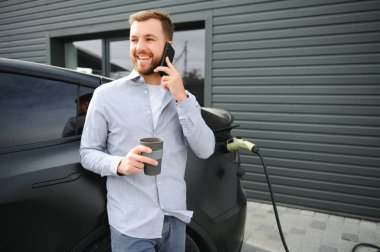 Evin yanında elektrikli araba şarj eden bir adam var..