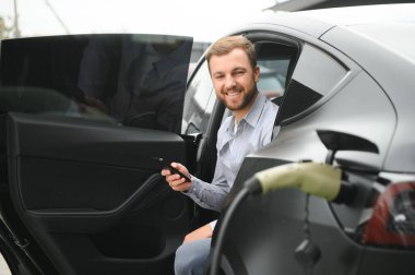 Bir adam elektrikli arabayı şarj eder..