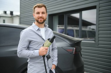 Dışarıdaki otoparkta elektrikli araba için elektrik kablosu tutan adam..