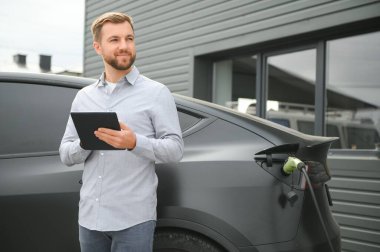 Bir adam elektrikli arabayı şarj eder..