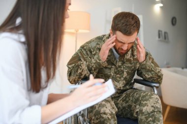 Kamuflaj üniformalı depresif adam tekerlekli sandalyedeki felç olmuş asker kadın psikoloğu ziyaret ediyor.