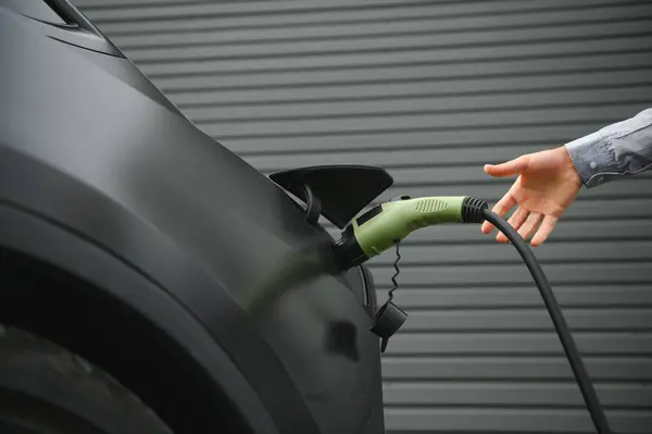 A man charges an electric car and checks the charge level on a smartphone.