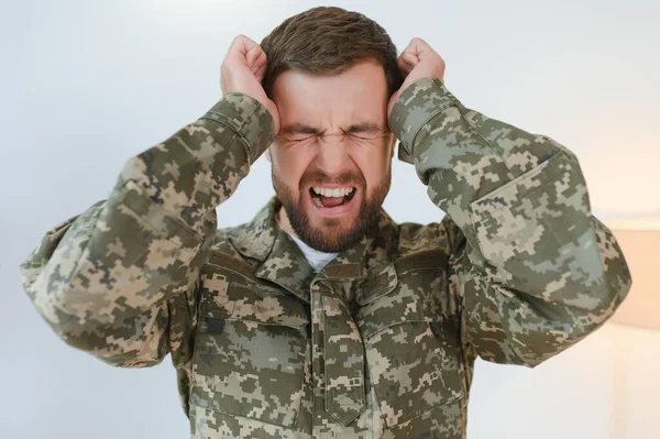 Closeup portrait of emotional young military man screaming and gesturing, sitting on couch at home and crying. Unhappy soldier visiting psychologist, suffering from posttraumatic stress, copy space.