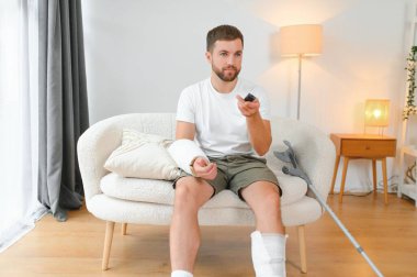 Evde araba kazası geçiren genç adam. Yaralı bir adam televizyon izliyor..