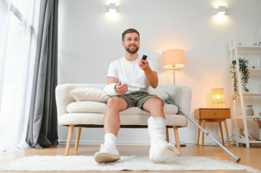 Evde araba kazası geçiren genç adam. Yaralı bir adam televizyon izliyor..