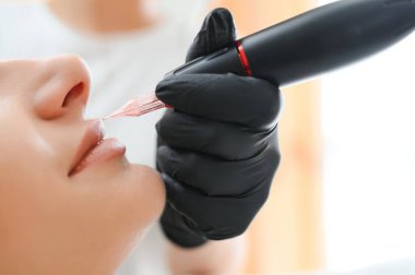 Banner Process kadını güzellik salonunda dudaklarına kalıcı dövme makyajı yapıyor..