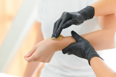 Şeker macunu tüy yolma prosedürü - karıştırma. Kozmetik uzmanı eline şeker yapıştırıcısı sürüyor..