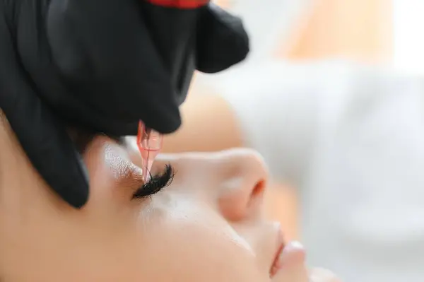 Permanent tattoo makeup on eyelashes of eyes of young woman in beauty salon.