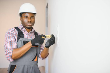 Genç erkek elektrikçi elektrik prizleri kuruyor ve değiştiriyor.