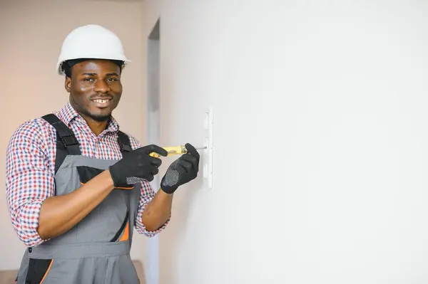 African-American electrician using socket voltage regulator in room.