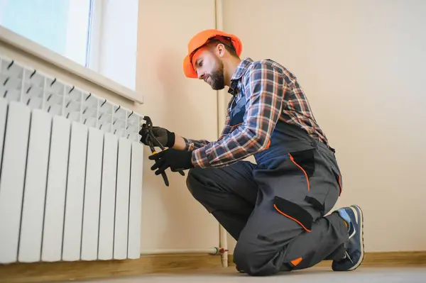 young man plumber checking radiator while installing heating system in apartment.