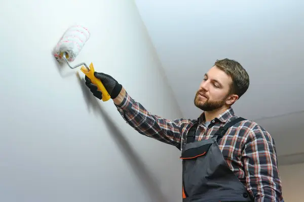 Painter painting a wall with paint roller. Builder worker painting surface with white color.