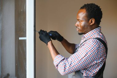 Evdeki oturma odasına plastik pencereler takan ya da ayarlayan Afro-Amerikan işçi..