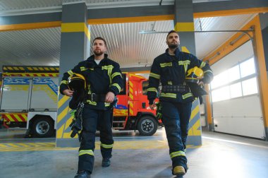 Two firefighters in protective clothing in helmets with fire engine. clipart