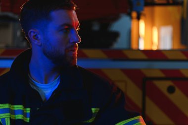 Görevdeyken itfaiyeci portresi. İtfaiyeci kasklı, itfaiye arabasının yanında..