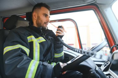 İtfaiye arabası süren koruyucu üniformalı itfaiyecinin yan görüntüsü..