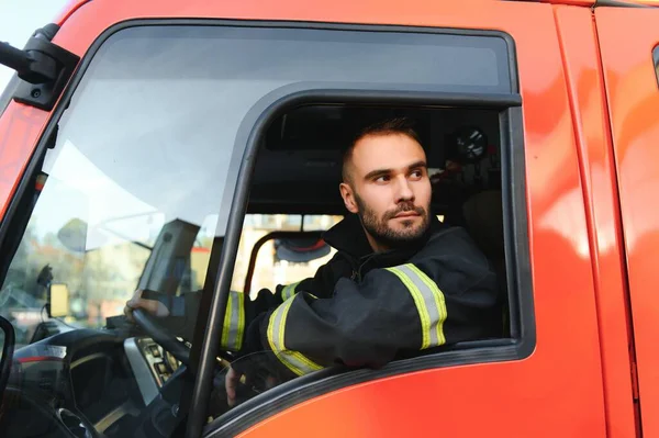 stock image Side view of firefighter in protective uniform driving fire engine.