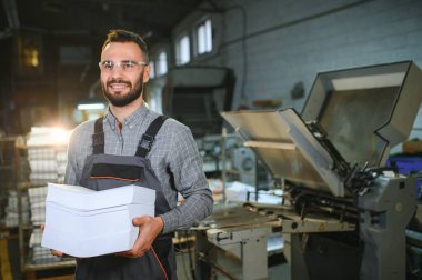 Çalışma üniformasında modern ofset baskı makinesi ve operatör ile ev içi yazdırma Kalite ve baskı süreci kontrol.