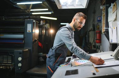 Yazıcı çalışanı yazdırma sürecinin kalitesini kontrol ediyor ve büyüteçle renkleri kontrol ediyor.