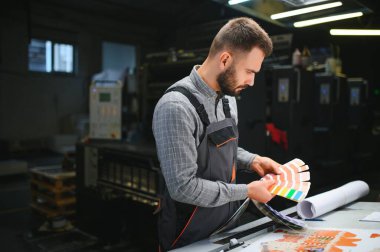 Yazıcı çalışanı yazdırma sürecinin kalitesini kontrol ediyor ve büyüteçle renkleri kontrol ediyor.