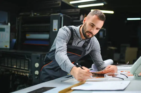 stock image Print house worker controlling printing process quality and checking colors with magnifying glass.