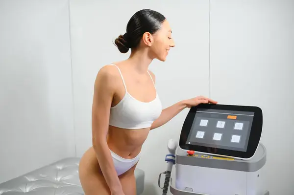 Young beautiful woman with laser hair removal machine in cosmetology cabinet.