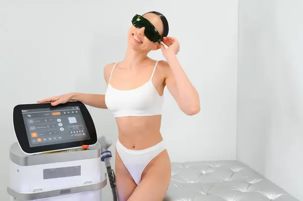 Young beautiful woman with laser hair removal machine in cosmetology cabinet.