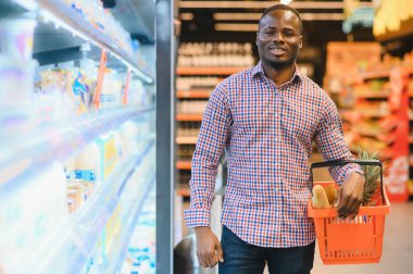 Afrikalı adam süpermarketten alışveriş yapıyor. Elinde alışveriş sepeti tutan yakışıklı adam..