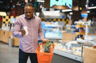 Afrikalı adam süpermarketten alışveriş yapıyor. Elinde alışveriş sepeti tutan yakışıklı adam..