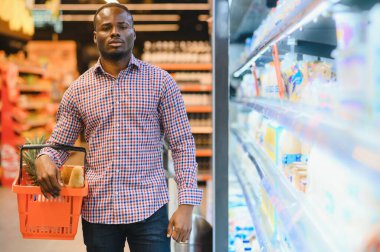 Süpermarkette gülümseyen adamın portresi. Markette elinde alışveriş sepeti olan genç bir Afrikalı..