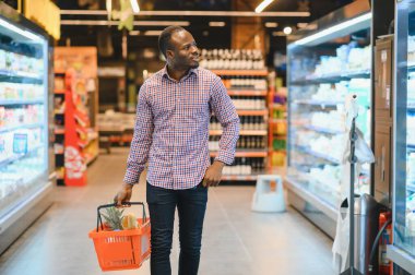 Afrikalı adam süpermarketten alışveriş yapıyor. Elinde alışveriş sepeti tutan yakışıklı adam..