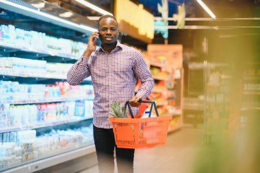 Afrikalı adam süpermarketten alışveriş yapıyor. Elinde alışveriş sepeti tutan yakışıklı adam..