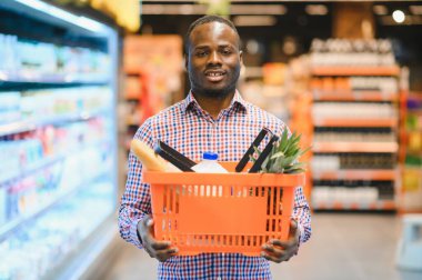Afrikalı adam süpermarketten alışveriş yapıyor. Elinde alışveriş sepeti tutan yakışıklı adam..