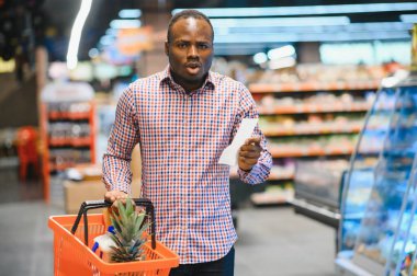Şaşırmış Afro-Amerikalı bir adam elinde kağıt torbayla toplam satış makbuzuna bakıyor..