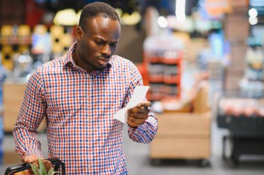 Şaşırmış Afro-Amerikalı bir adam elinde kağıt torbayla toplam satış makbuzuna bakıyor..