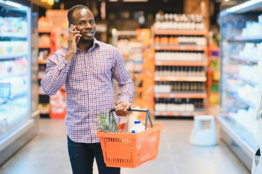 Süpermarkette alışveriş yaparken cep telefonuyla konuşan Afrikalı Amerikalı adam..
